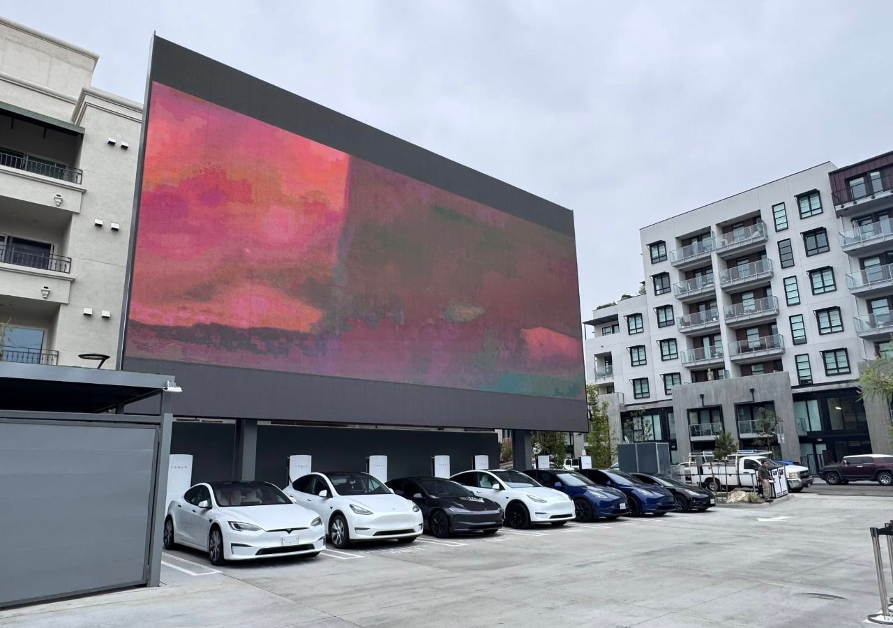 Voitures électriques garées sous un grand écran publicitaire.
