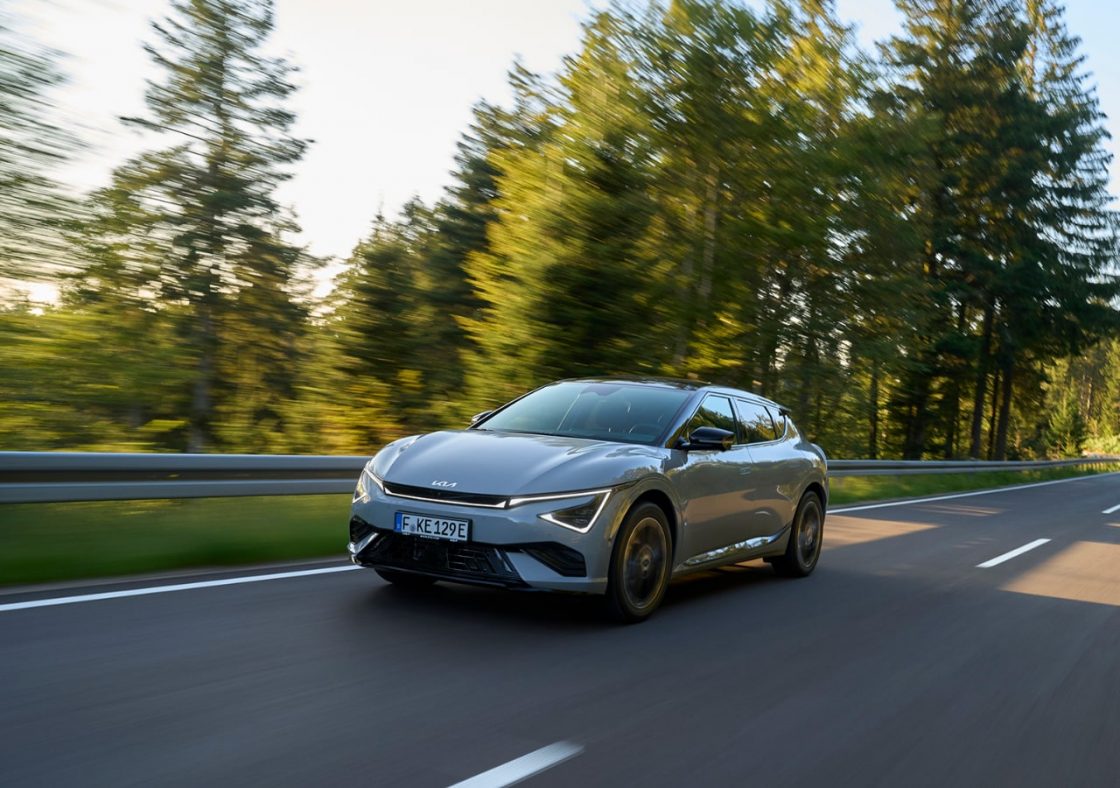Voiture grise électrique roulant sur route entourée de forêts.